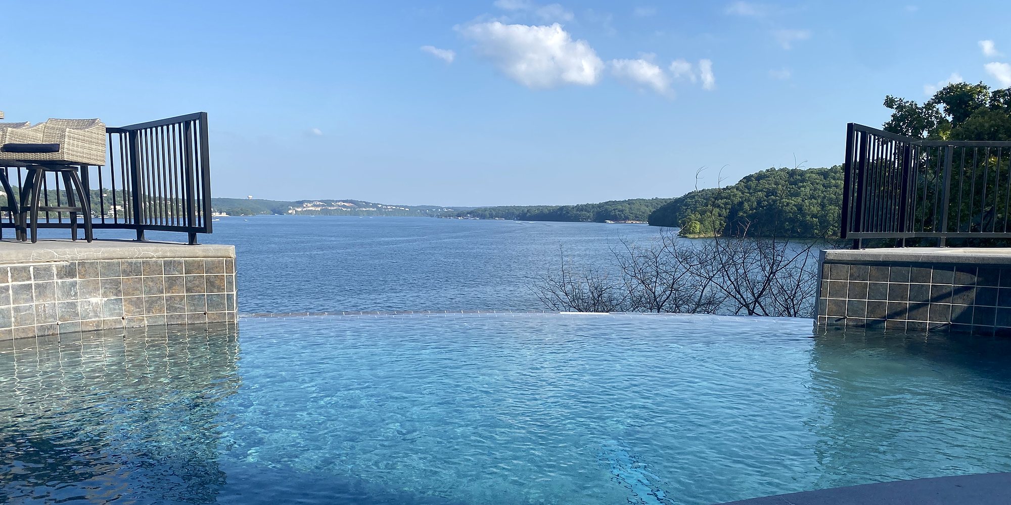 An infinity pool looking out over a lake and wooded hills on a clear summer afternoon