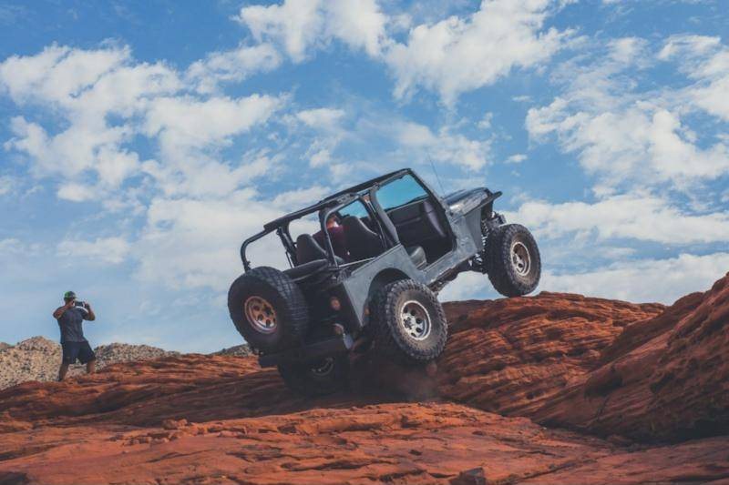 An off-road vehicle climbing a steep face of red slickrock while a spotter watches