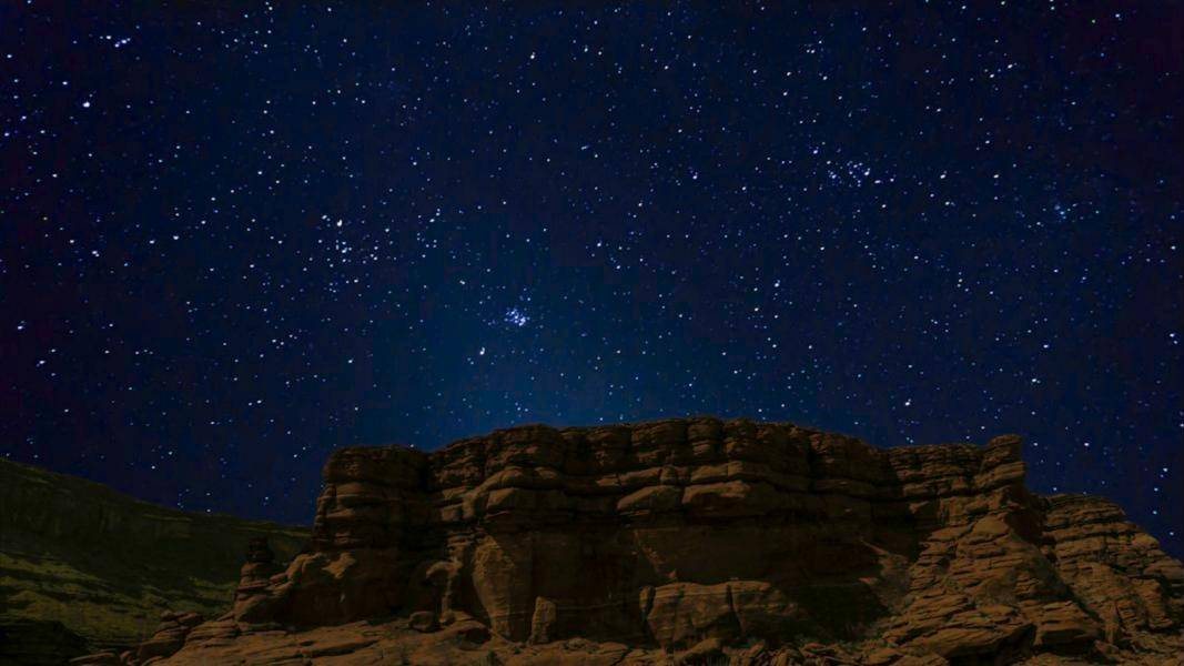 A sky full of stars above a red rock formation at night